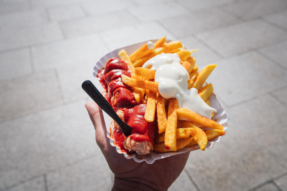 Hand holding a plate of fries with ketchup and mayonnaise, outdoors