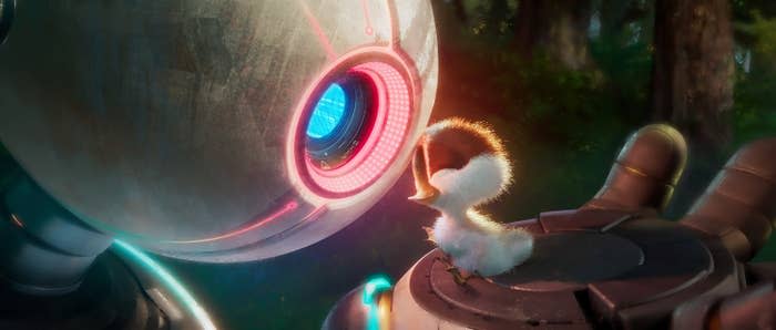 A small fluffy bird interacts with a large, round robot with a glowing eye in a forest setting