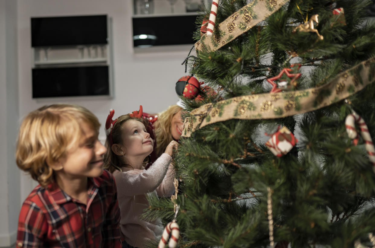 kids with mom putting up the christmas tree lights - focus on little girl -