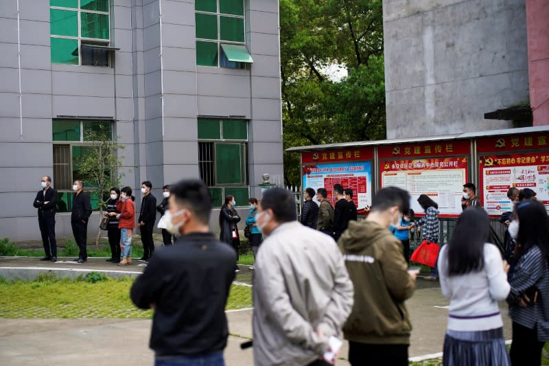 Varias personas con máscaras faciales hacen cola frente a un centro de salud comunitario para realizar pruebas de ácido nucleico en Xianning