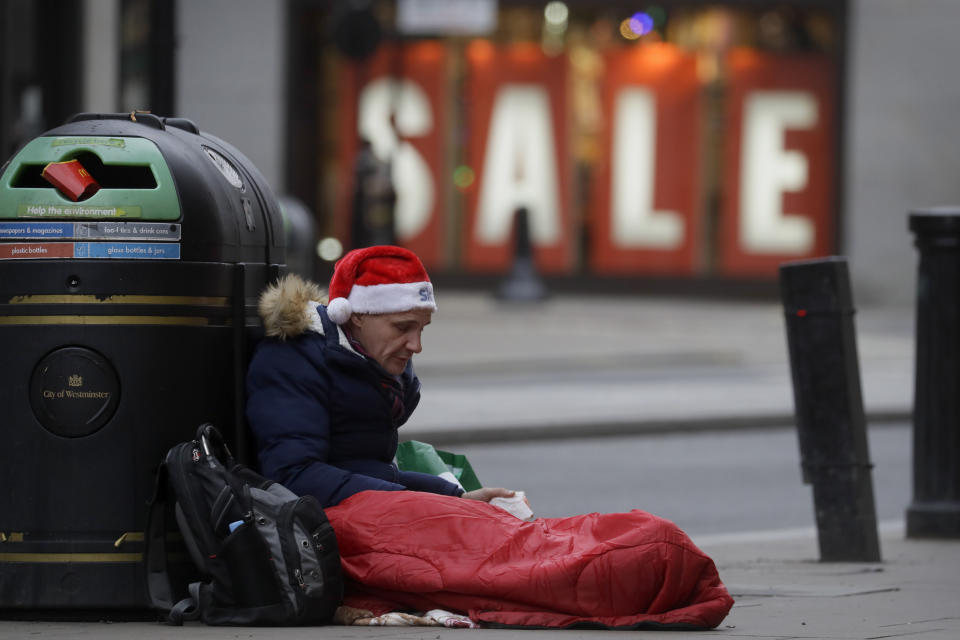 A homeless man wears a santa hat as he sits on Oxford Street in London, Saturday, Dec. 26, 2020. London is currently in Tier 4 with all non essential retail closed and people have been asked to stay at home, on what is usually one of the busiest retail days of the year with the traditional Boxing Day sales in shops. (AP Photo/Kirsty Wigglesworth)