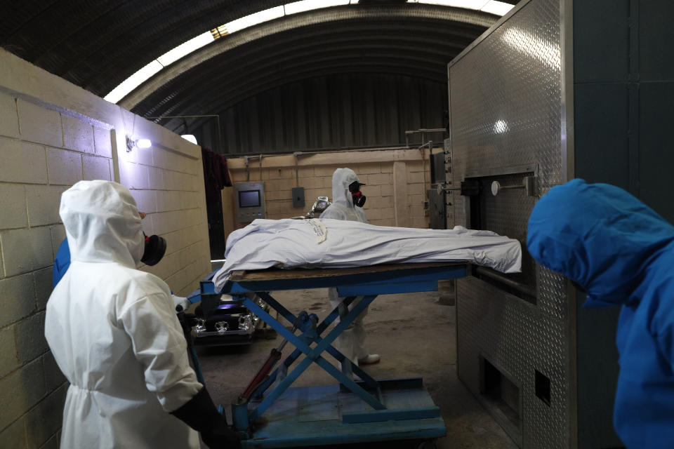 Trabajadores con equipo de protección meten a un horno el cuerpo de una persona que murió de complicaciones derivadas del coronavirus, para cremarlo, el jueves 21 de mayo de 2020 en el Mausoleo San Cristóbal en Ecatepec, México. (AP Foto/Rebecca Blackwell)