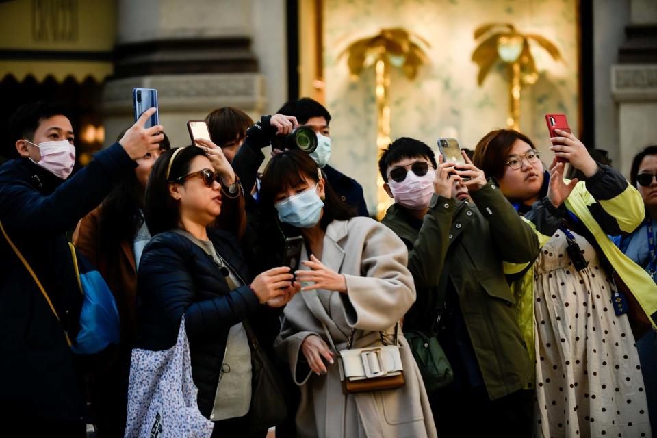 People wearing sanitary masks take photos in central Milan (AP)