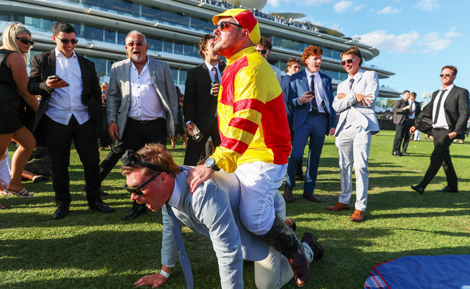 A man wearing a jockey costume, pictured here riding another man at the Victoria Derby.