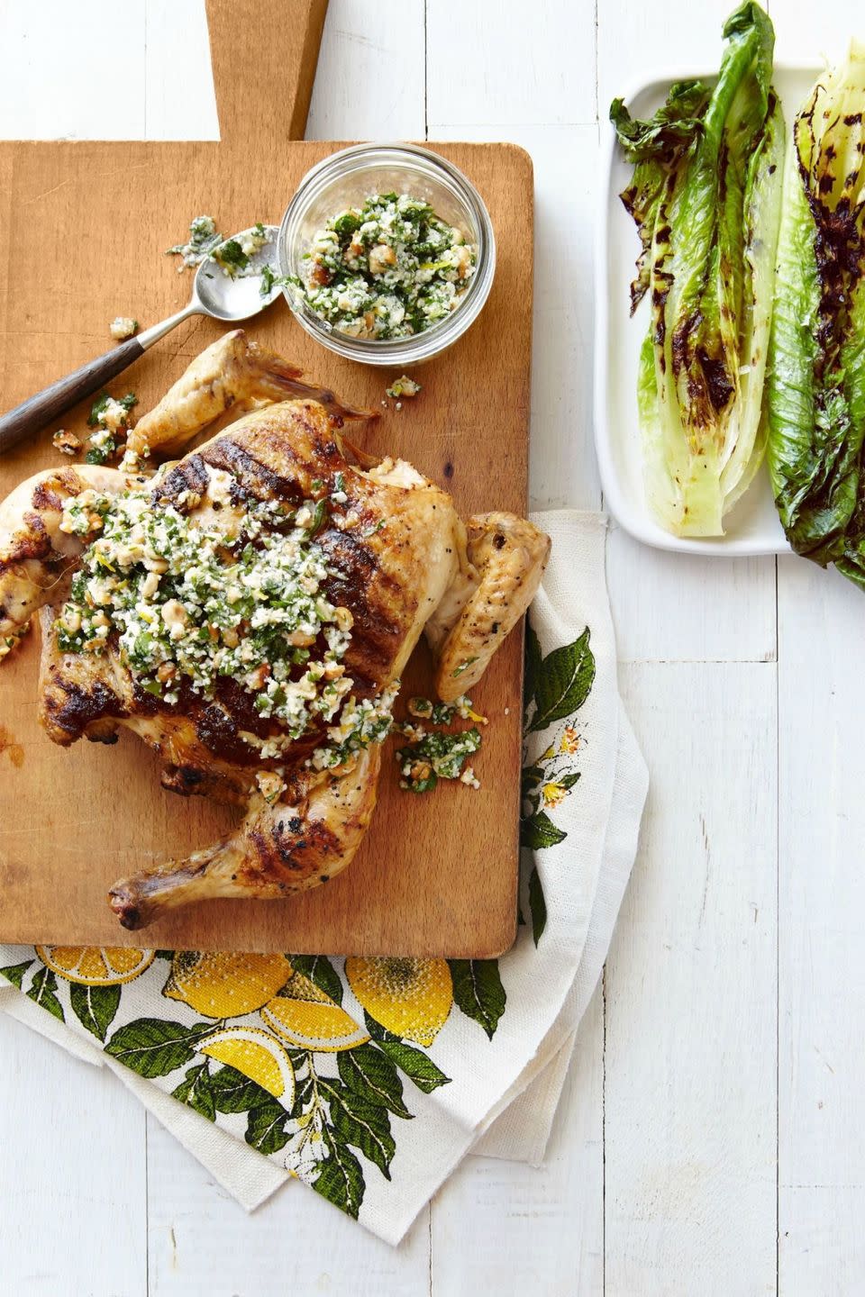 flattened chicken on a wooden serving board with grilled romaine and parsley lemon sauce