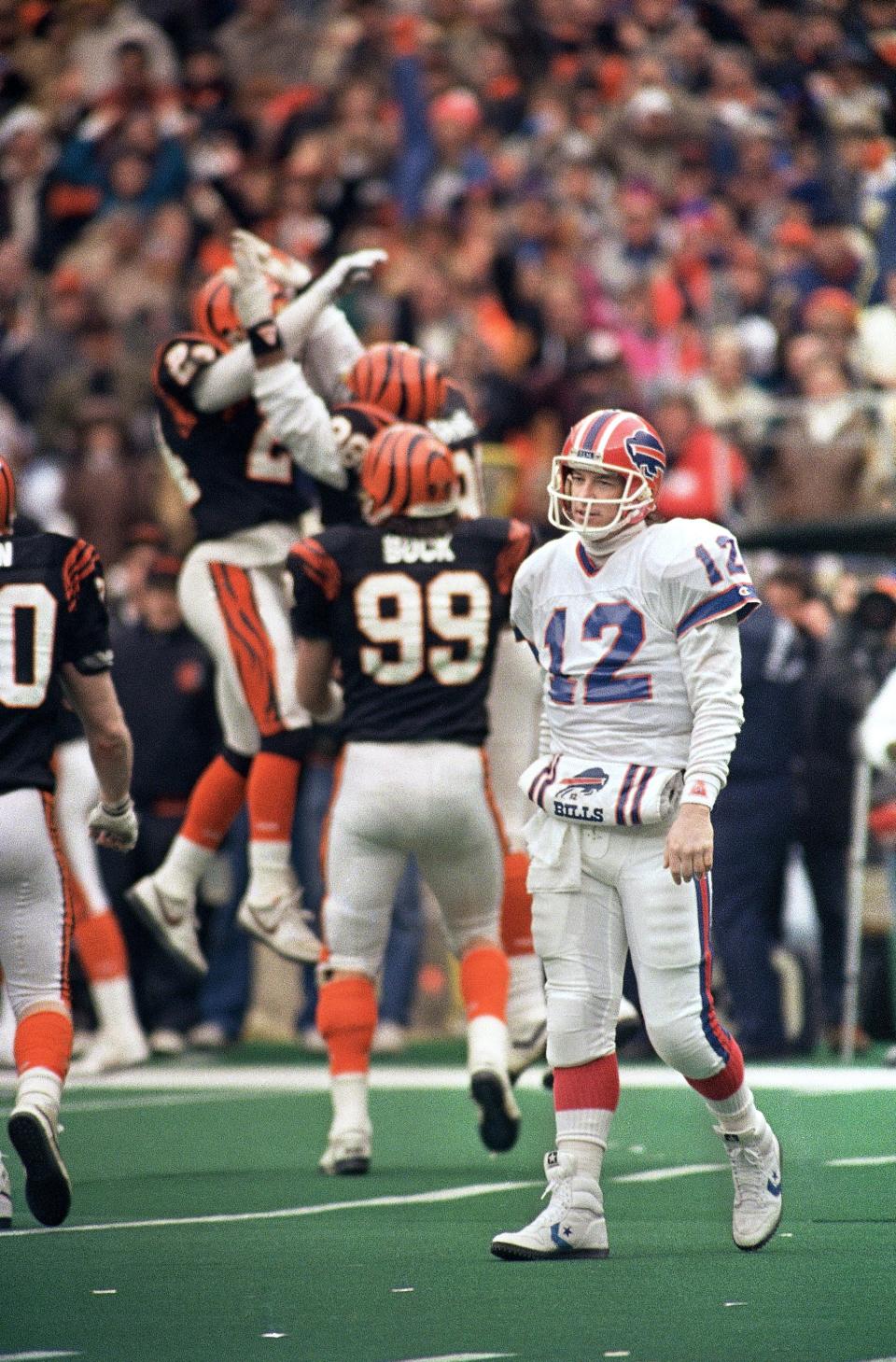 Buffalo Bills quarterback Jim Kelly (12) walks off the field as Cincinnati Bengals defenders Jason Buck (99), Lewis Billups (24) and David Grant (98) celebrate a 10-yard sack in the second quarter of the AFC Championship game, Sunday, Jan. 8, 1989 in Cincinnati, Ohio.