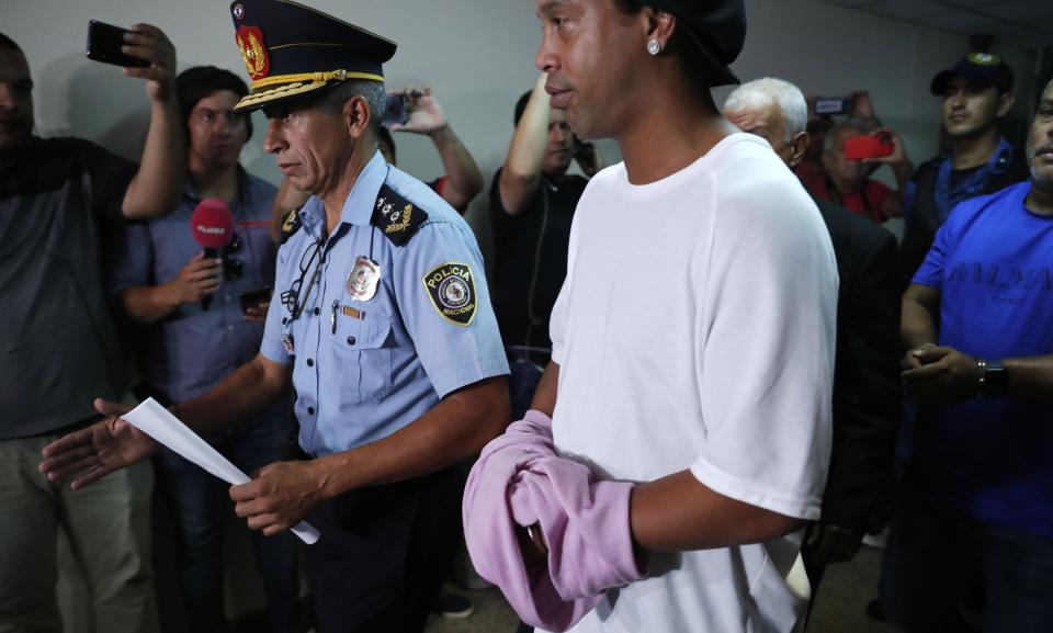 Former soccer star Ronaldinho talks as he walks escorted by Police officers with hands handcuffed to declare to judge Clara Ruiz Diaz at Justice Palace in Asuncion, Paraguay, Saturday, March 7, 2020. Ronaldinho and his brother Roberto de Assis Moreira, right back, were alleged to enter to the country with a false Paraguayan passport.(AP Photo/Jorge Saenz)