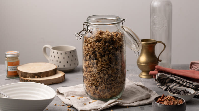 granola in a glass container surrounded by cookware