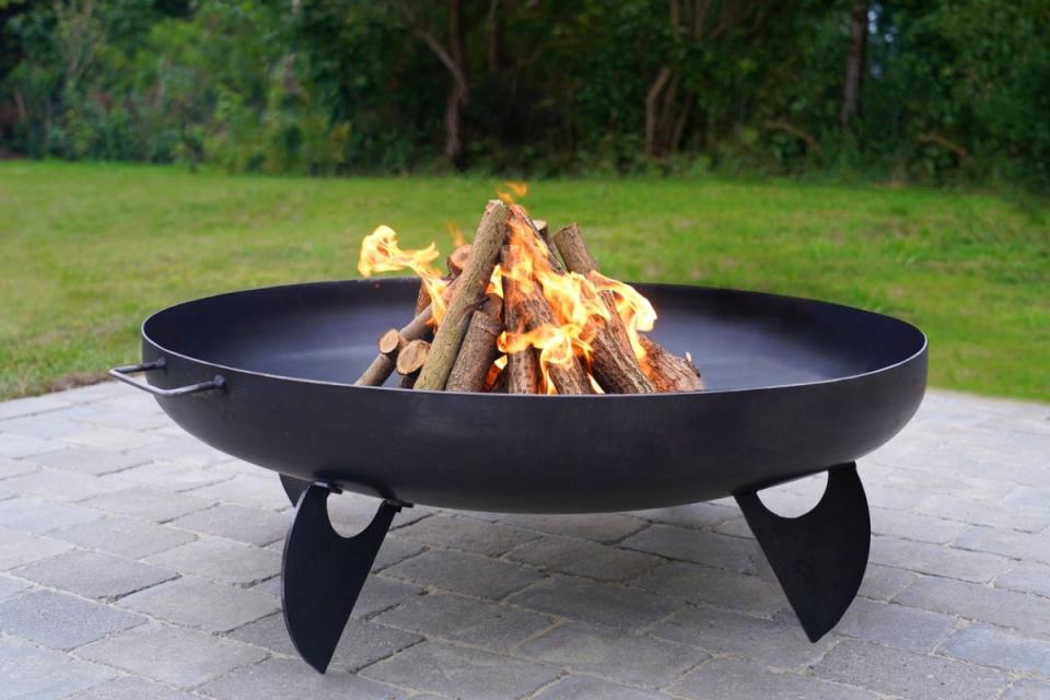 Metal fire pit with burning fire on a grey stone patio