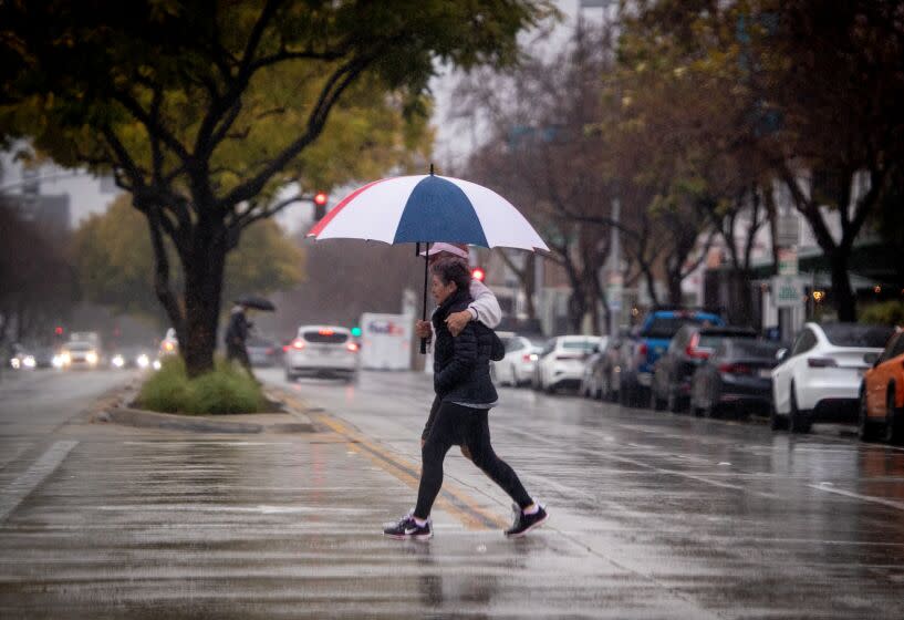 Pasadena, CA - February 24: Pedestrians toting an umbrella walk across the street amidst heavy rain in Pasadena on Friday, Feb. 24, 2023 in North Hollywood,. Southern California has only gotten a taste of the powerful winter storm system that forecasters say will bring an extended period of cold temperatures, high winds and snow, prompting the region's first blizzard warning on record.(Allen J. Schaben / Los Angeles Times)