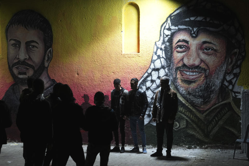 Palestinians take photos of themselves in front of a mural painting of the late Palestinian president Yasser Arafat, right, and late Nasser Abu Hamid, left, a veteran Palestinian prisoner who died from lung cancer in Israeli custody, in preparation of celebration of 58th Fatah anniversary, at the main square in Gaza City, Friday, Dec. 30, 2022. (AP Photo/Adel Hana)