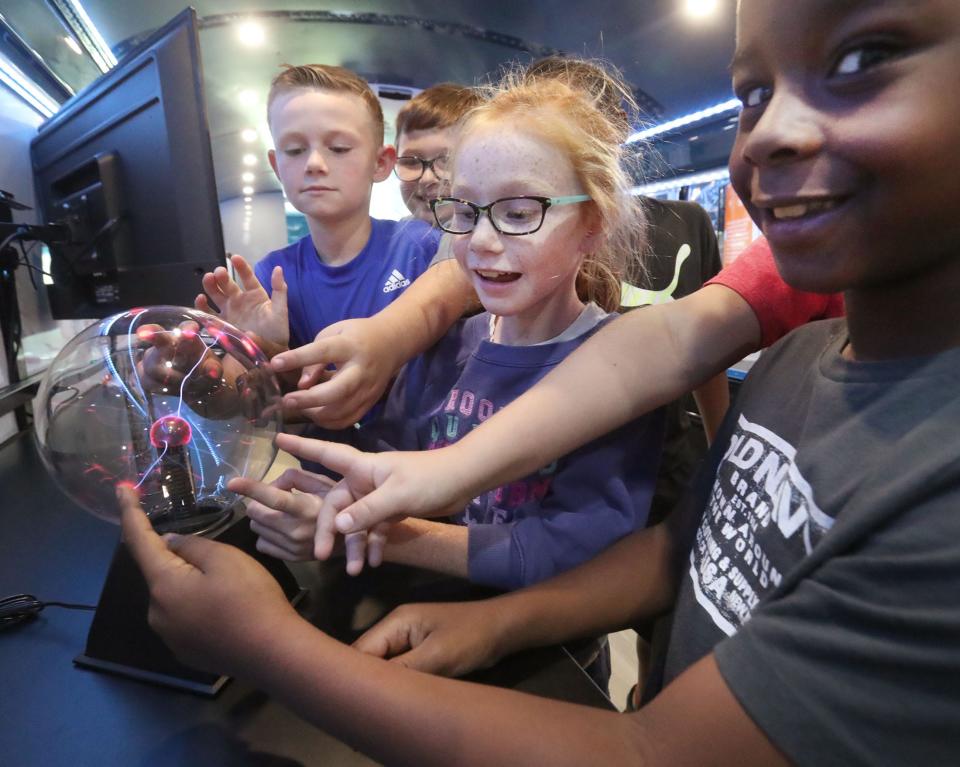 From left, Beachside Elementary students Aaron Dye, Tyler Annon, Michaela Smurdon and Senai Miller react as colorful strands of light are drawn to their fingers as they touch a Plasma Ball, Tuesday, Oct. 3, 2023, while touring Volusia County Schools' new STEM bus.