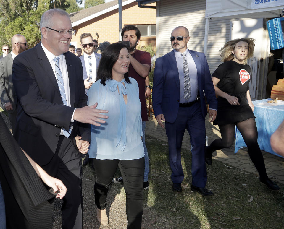 Australian Prime Minister Scott Morrison, left, holds his wife Jenny's hand as an anti-coalmining protester runs in from the right after Morrison voted in a federal election in Sydney, Australia, Saturday, May 18, 2019. Political leaders continued frenetic 11th-hour campaigning as Australians vote on Saturday in an election likely to deliver the nation's sixth prime minister in as many years. (AP Photo/Rick Rycroft)