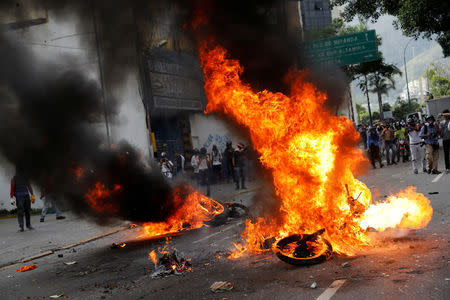 Demonstrators look on as motorcycles belonging to riot security forces are set on fire during a rally against Venezuela's President Nicolas Maduro in Caracas, Venezuela. REUTERS/Carlos Garcia Rawlins