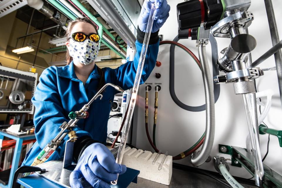 A woman works with a blow torch and glass tube