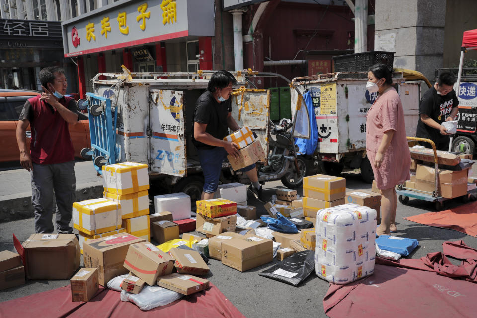 A woman wearing a protective face mask to help curb the spread of the new coronavirus waits for a delivery worker sorting out her parcel at a collection point outside an apartment in Beijing, Sunday, June 21, 2020. According to state media reports, nearly one hundred thousand delivery workers have to accept the nucleic acid testing, a countermeasure to prevent the spread of the virus in the capital city. (AP Photo/Andy Wong)