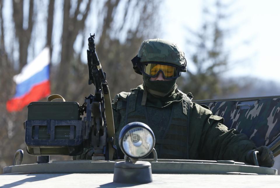 Military personnel, believed to be a Russian serviceman, stands guard on military vehicle outside the territory of a Ukrainian military unit in the village of Perevalnoye outside Simferopol