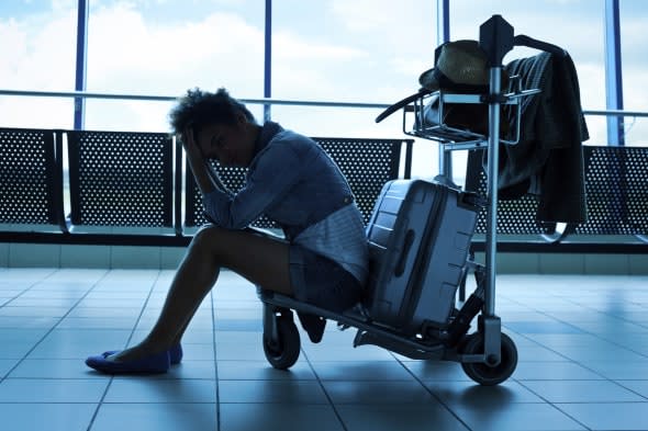 A bored teenage girl sitting on a luggage trolley at the airport and waiting for her flight. Dark tones.