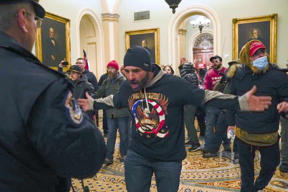 FILE - Trump supporters, including Doug Jensen, center, confront U.S. Capitol Police in the hallway outside of the Senate chamber, Jan. 6, 2021, at the Capitol in Washington. A trial is set to open for Jensen, who ran after a police officer retreating up a flight of stairs during a mob's attack on the U.S. Capitol, a harrowing encounter captured on video. Jensen, who wore a shirt promoting the QAnon conspiracy theory, told the FBI that he wanted to be a "poster boy" for the events that unfolded on Jan. 6, 2021. (AP Photo/Manuel Balce Ceneta, File)