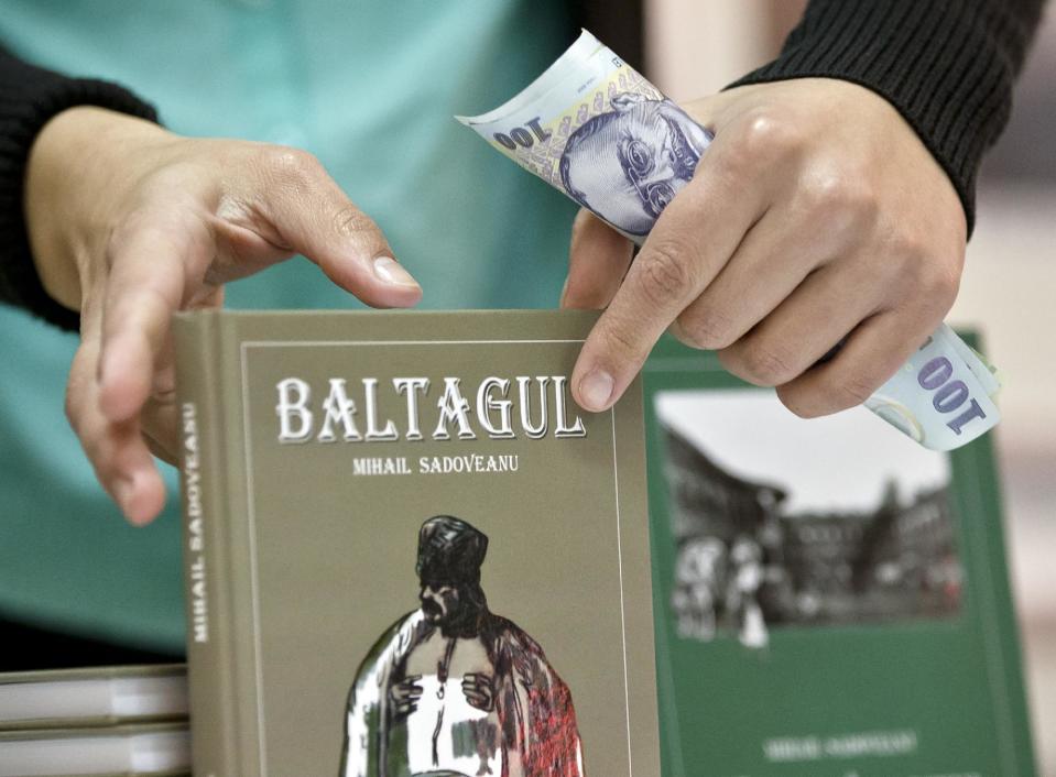 In a Nov. 14, 2013, photo, a woman holds money while selling republished novels by Romanian writer Mihail Sadoveanu in Bucharest, Romania. He is one of Romania’s greatest writers, but his work couldn’t be found in bookstores. Now, they are finally getting their place back on the shelf. (AP Photo/Vadim Ghirda)