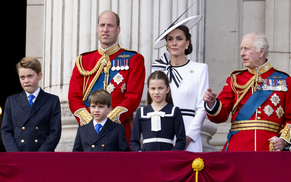 Prince George, Prince Louis, Prince William, Princess Charlotte, Kate Middleton, and King Charles stand on a balcony wearing formal attire for a public event