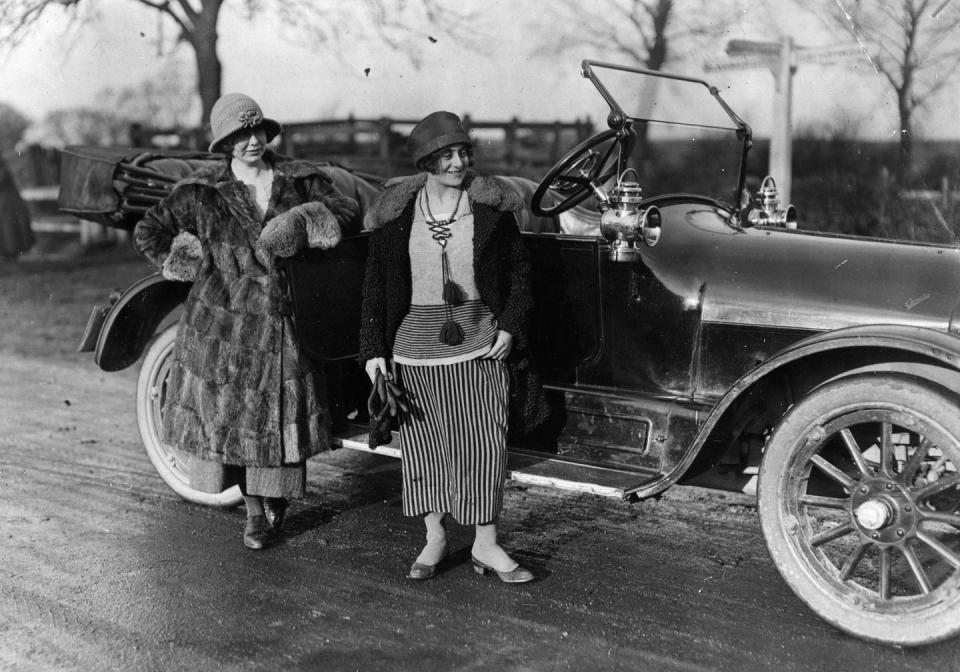 <p>Two women enjoy a luxe lifestyle, donning fur coats while posing next to a new car.</p>