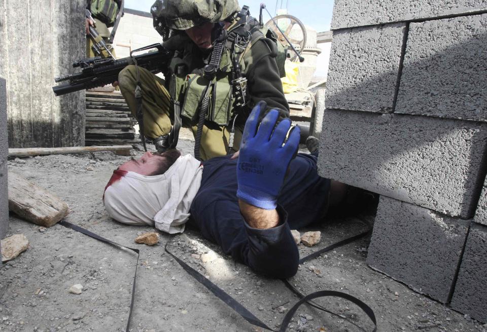 An Israeli soldier kneels next to an injured Jewish settler who was detained by Palestinian villagers near Nablus