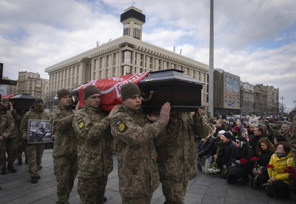 People kneel as servicemen carry the coffins of four Ukrainian soldiers, who were part of a reconnaissance group and were killed on Dec. 25 in Russia as they performed a special task, during a commemoration ceremony in Independence Square in Kyiv, Ukraine, Tuesday, March 7, 2023. The servicemen names are Bohdan Legov, 19, Maksym Mykhailov, 32, Yuri Horobets, 34, Taras Karpiuk, 36. (AP Photo/Efrem Lukatsky)