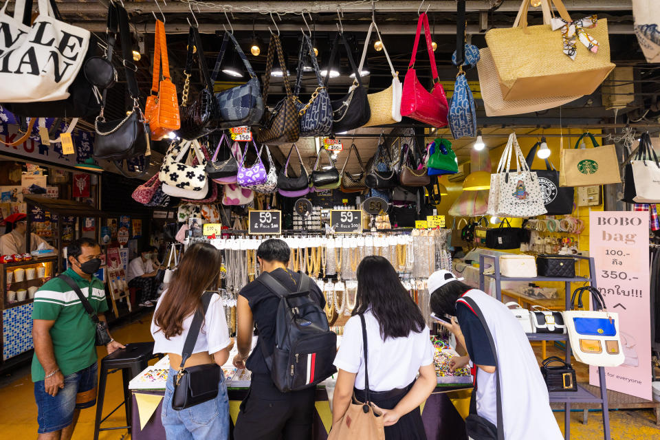 Image shows five people, men and women, shopping at a Thai store selling bags. 