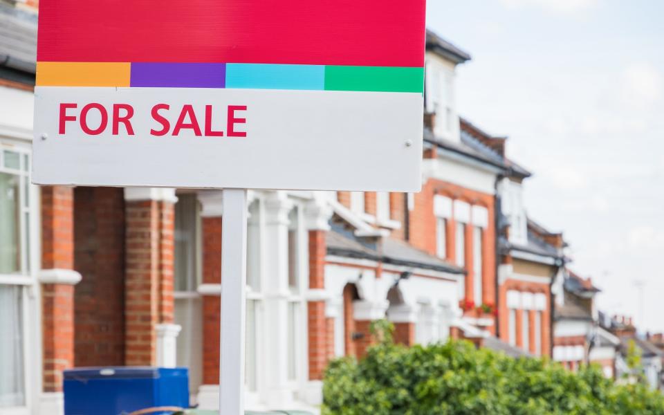 For Sale estate agent sign displayed outside a terraced house