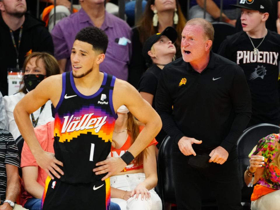 Robert Sarver (right) yells from the crowd as Phoenix Suns star Devin Booker reacts on the court.