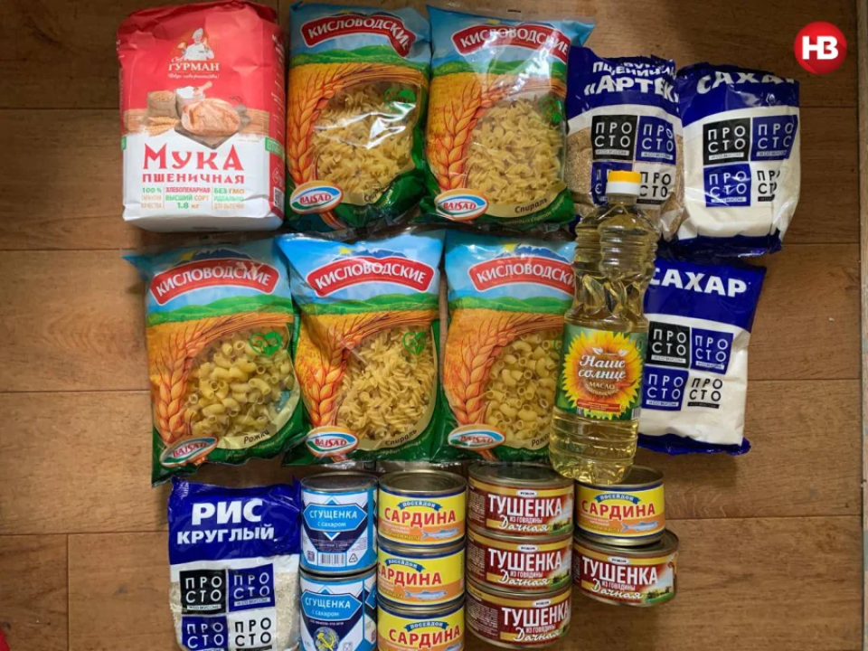 Visible on the photograph are 5 packages of macaroni, made in the Russian town of Kislovodsk, 1 package of Gurman-brand flour (1.8kg), 1 package each of Artek wheat groats and rice, 2 packages of sugar, 1 liter of sunflower oil, 2 cans of sugary condensed milk, 4 cans of canned fish, and 4 cans of canned stewed beef. <span class="copyright">NV</span>