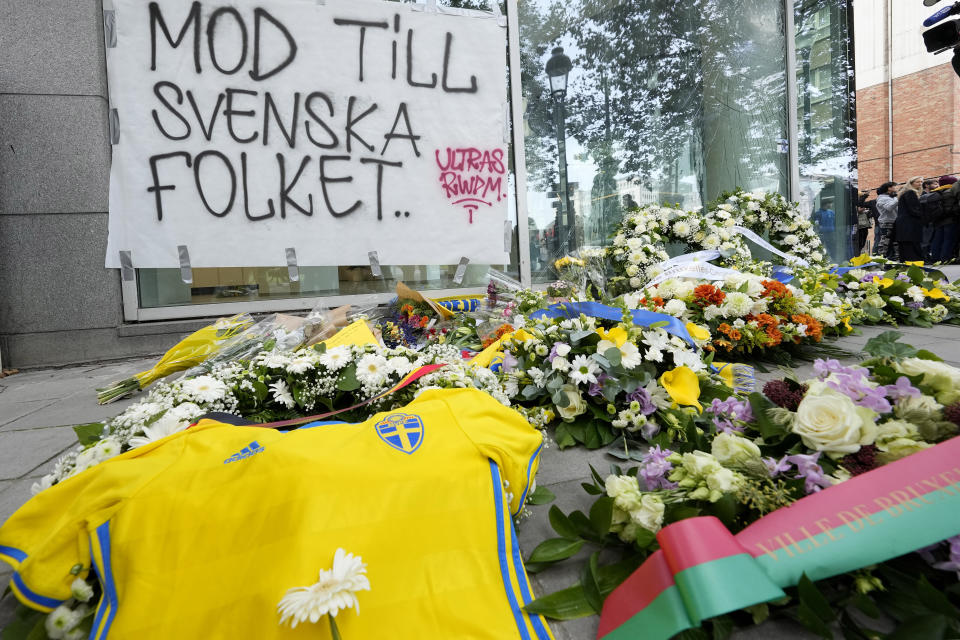 Floral tributes, a Swedish team jersey, and notes of condolence are placed on the pavement and a sign reads 'courage to the Swedish people' during a commemoration for the victims of a shooting in the center of Brussels, Wednesday, Oct. 18, 2023. Police in Belgium on Tuesday shot dead a suspected Tunisian extremist accused of killing two Swedish soccer fans in a brazen attack on a Brussels street. (AP Photo/Martin Meissner)