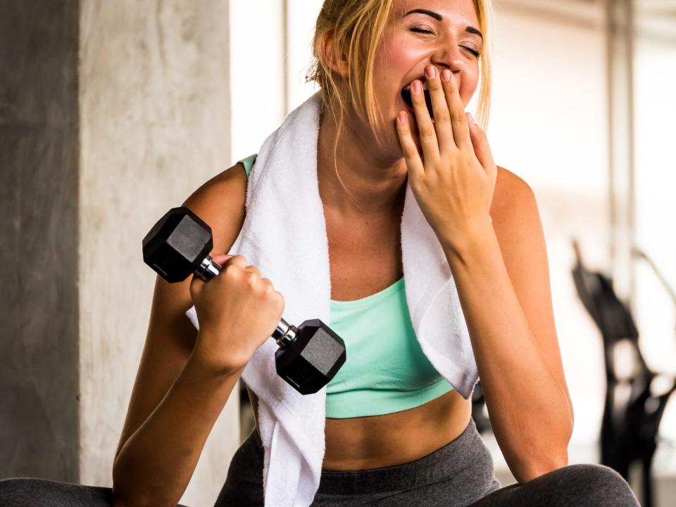 a woman athlete yawning while lifting light dumbbell weights in the gym