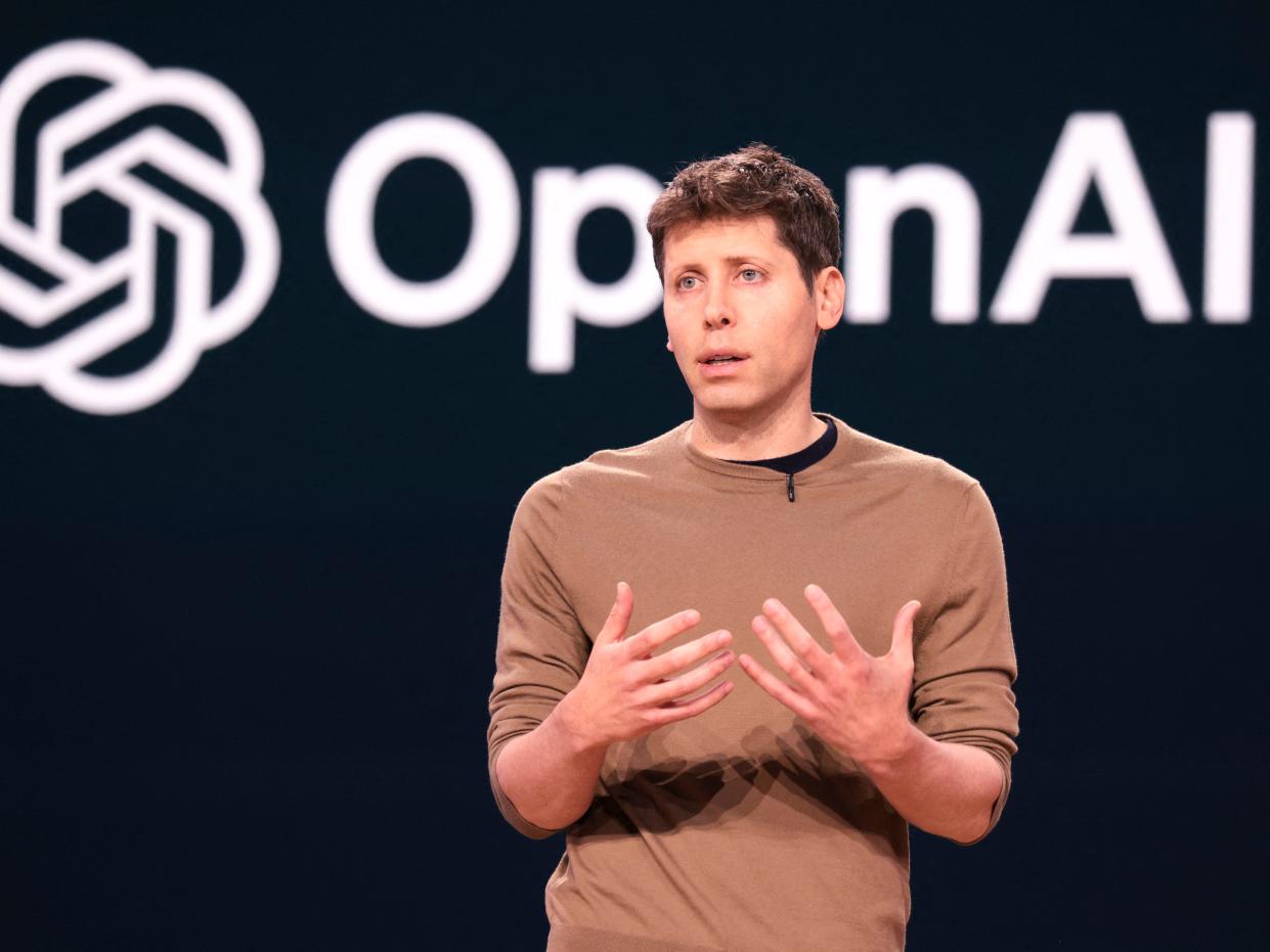 Sam Altman presenting onstage with the OpenAI logo behind him.