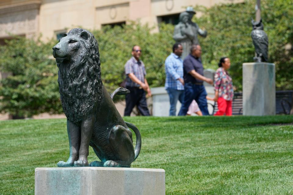 Visitors pass by the lion sculpture by artist Jack Greaves in Battelle Riverfront Park that is part of the Scioto riverfront art walk Downtown.