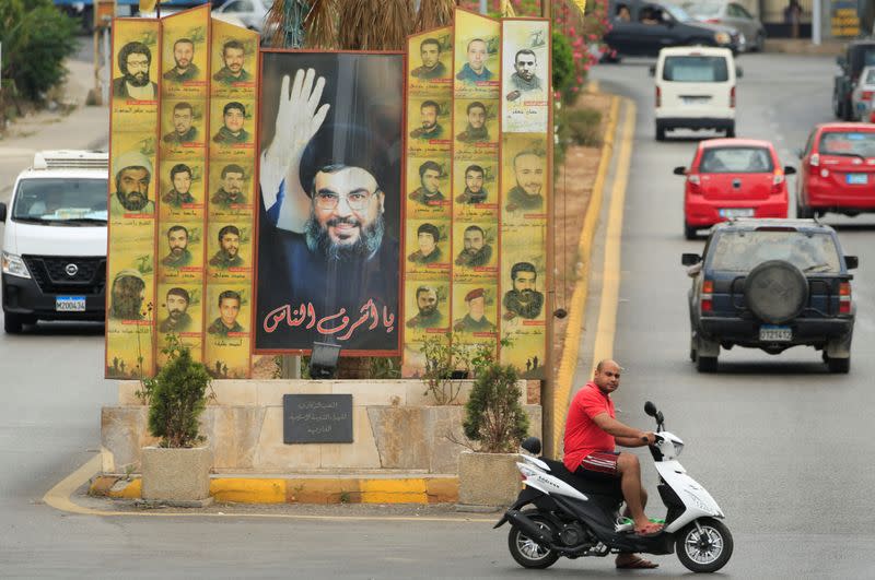 A man rides a motorbike past a poster depicting Lebanon's Hezbollah leader Sayyed Hassan Nasrallah