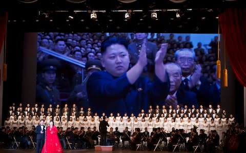 Kim Jong Un is projected on a screen behind an orchestra and choir during a performance in Pyongyang, North Korea - Credit: AP Photo/David Guttenfelder