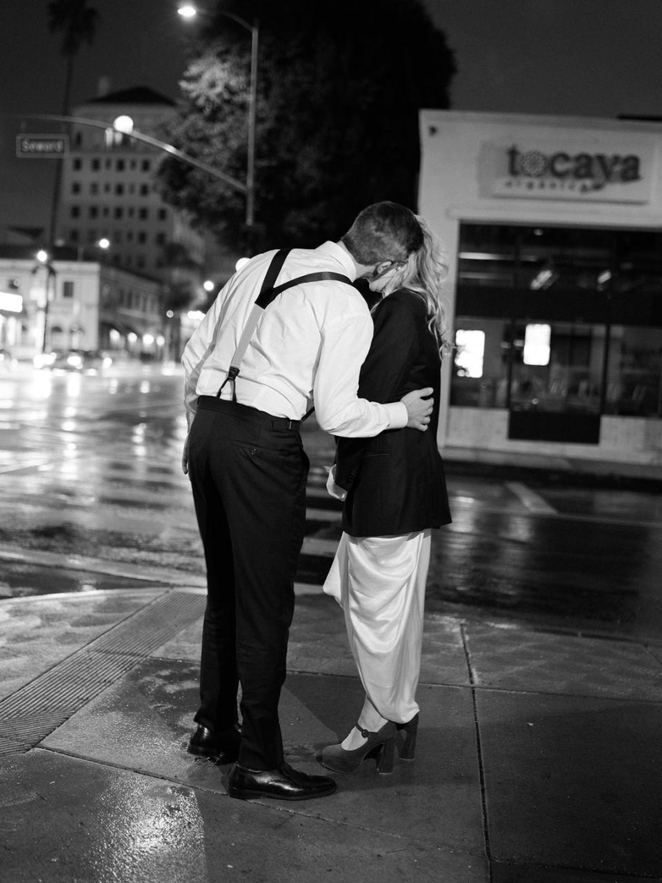 a man and woman kissing on a sidewalk at night