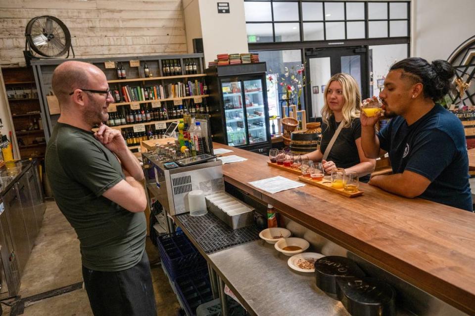 Bartender Jerome Luther explains different flights of wine to customers Alexandro Morales and Mary Bondar inside Lucid Winery in midtown Sacramento on Wednesday, July 12, 2023. One was a traditional flight of wine with one infused with hibiscus and the other flight was called Dealers Choice. “For Dealers Choice, we do the thinking, they do the drinking,” said Luther.