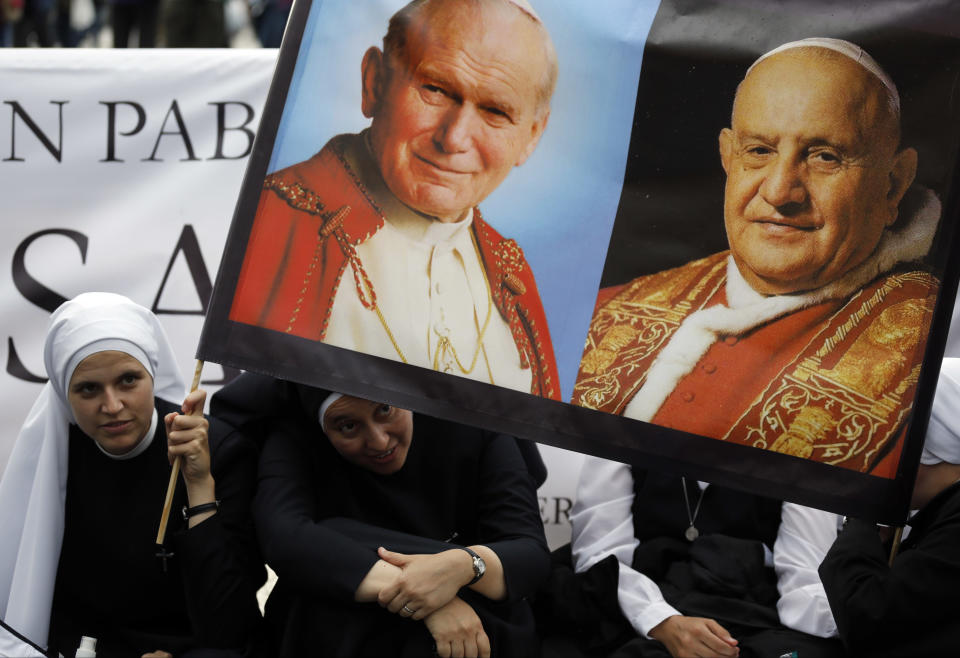 Nuns hold up pictures of late Pope John Paul II, top left, and Pope John XXIII, in St. Peter's Square at the Vatican, Saturday, April 26, 2014. Pilgrims and faithful are gathering in Rome to attend Sunday's ceremony at the Vatican where Pope Francis will elevate in a solemn ceremony John XXIII and John Paul II to sainthood. (AP Photo/Alessandra Tarantino)