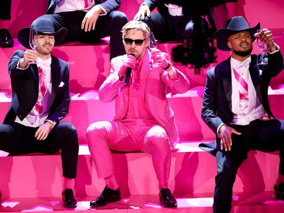 Ryan Gosling singing in a pink suit, holding up a Champagne glass, with dancers around him.