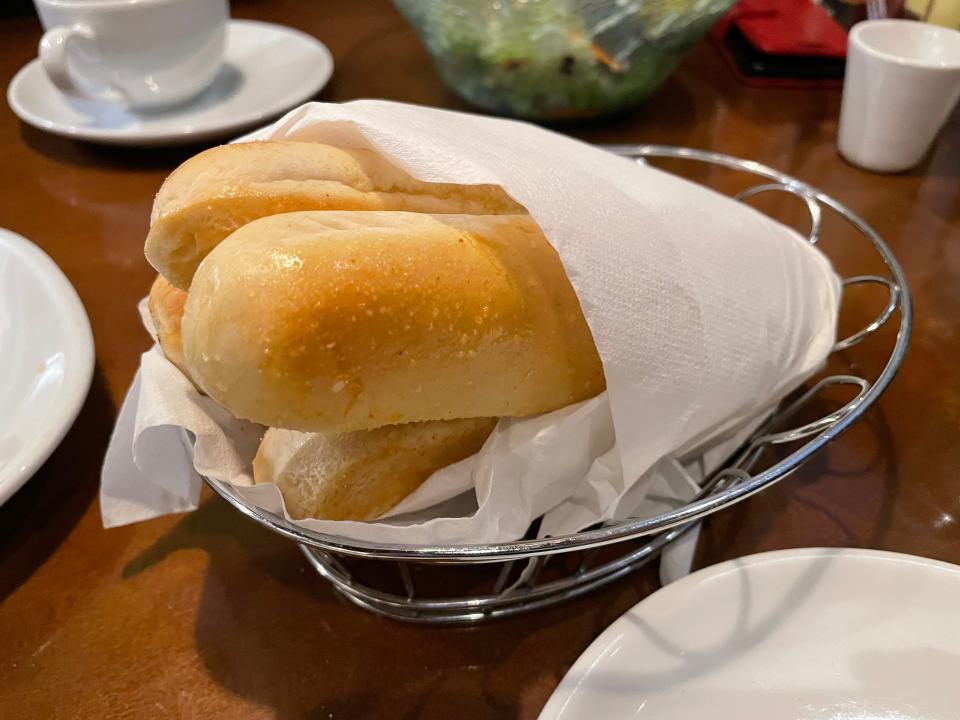 Bundle of light-brown breadsticks sit wrapped in paper in a metal bread basket