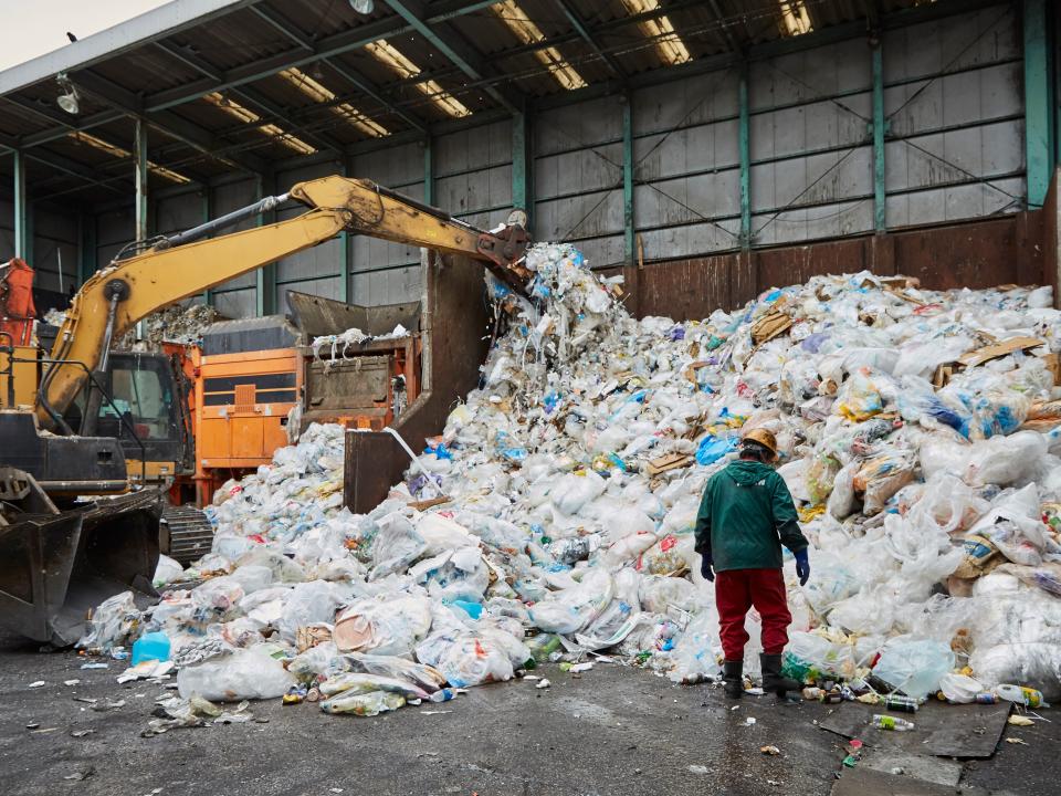 A worker stands in front of a pile of plastic waste as machinery processes it at a facility in Japan.