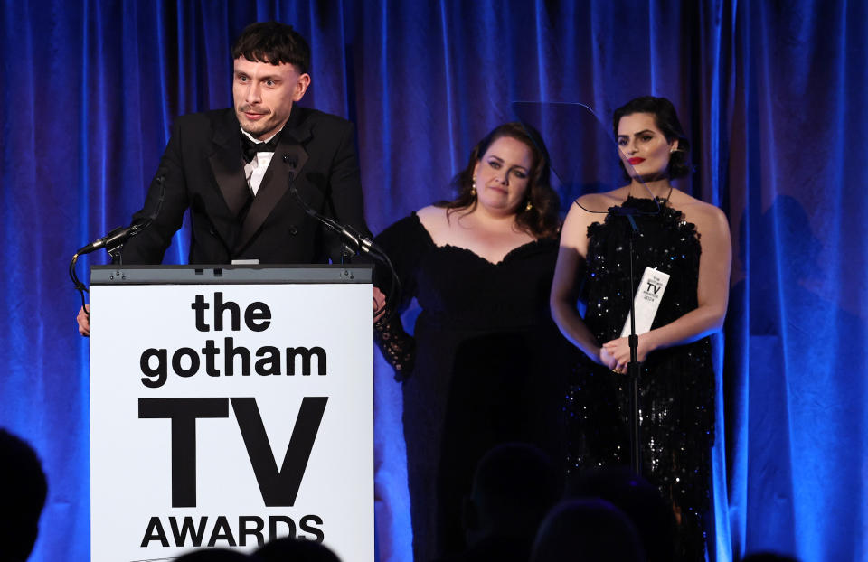 Writer and actor Richard Gadd wearing a tuxedo and speaking at a podium for The Gotham TV Awards, with costars Jessica Gunning and Nava Mau behind him.