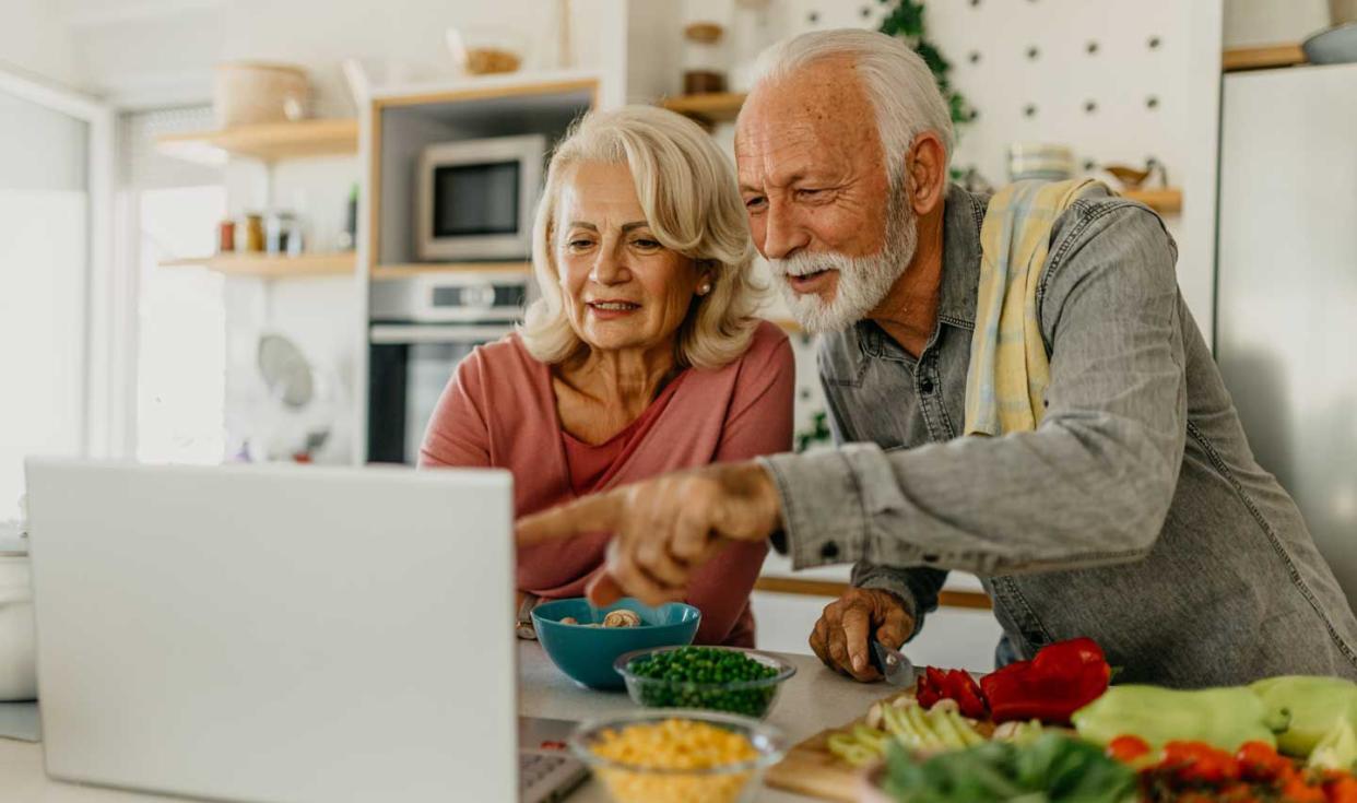 Elderly couple looking at laptop while cooking