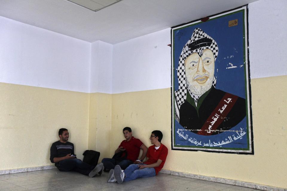 In this Wednesday, April 9, 2014 photo, Palestinians students sit next to a picture of late Palestinian leader Yasser Arafat at the Al-Quds University in the West Bank village of Abu Dis, near Jerusalem. Dozens of Palestinian doctors who graduated from Al-Quds University, a school that has a foothold in east Jerusalem, are caught in the political battle between Israel and the Palestinians over the city’s eastern sector. Israel has refused to recognize the university’s graduates -- a move that could amount to acknowledging the Palestinian claims to east Jerusalem as their capital. Arabic on picture reads, "Faculty of Medicine, martyr, leader Yasser Arafat, Al-Quds University." (AP Photo/Majdi Mohammed)