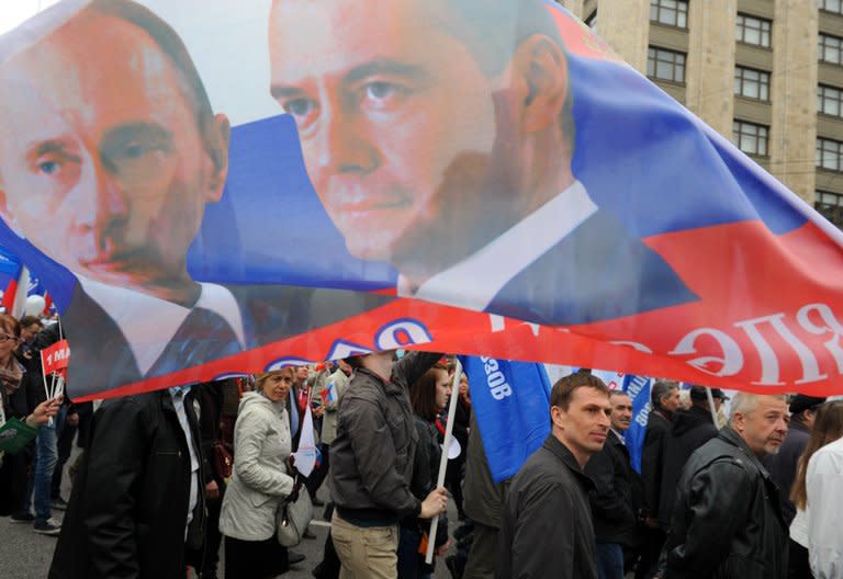 People carry a banner with portraits of Russia's President Vladimir Putin (L) and Prime Minister Dmitry Medvedev during traditional May Day Trade Unions rally in central Moscow on May 1, 2013. When Putin returned one year ago to the Kremlin, Russia could boast robust if unspectacular growth, but in just 12 months, growth has slipped to the extent that Russia risks entering recession