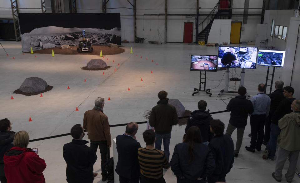 Guests and media watch as astronaut Luca Parmitano of Italy, seen on screen, remote controls the Space Rover, rear, which successfully picked up a rock during a training exercise of the European Space Agency, ESA, in Katwijk, near The Hague, Netherlands, Monday, Nov. 25, 2019. (AP Photo/Peter Dejong)