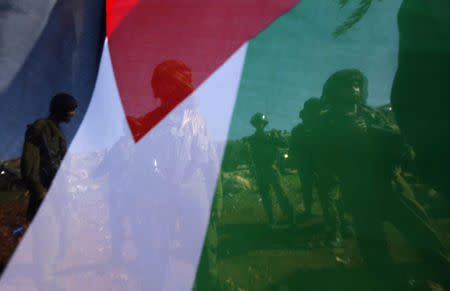 Israeli soldiers are pictured through a Palestinian flag as they stand guard during a protest by Palestinians against Jewish settlements near the West Bank city of Ramallah December 10, 2014. REUTERS/Mohamad Torokman